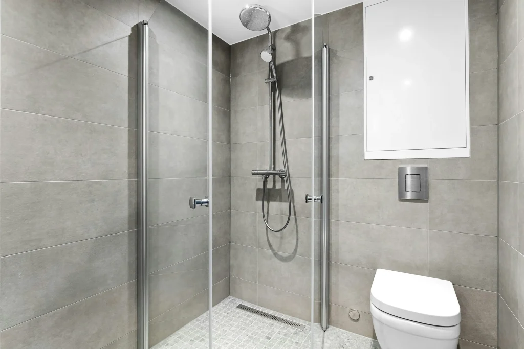 Complete walk-in shower transformation featuring custom gray stone wall panels, a seamless glass panel partition, and a minimalist low-profile shower base.