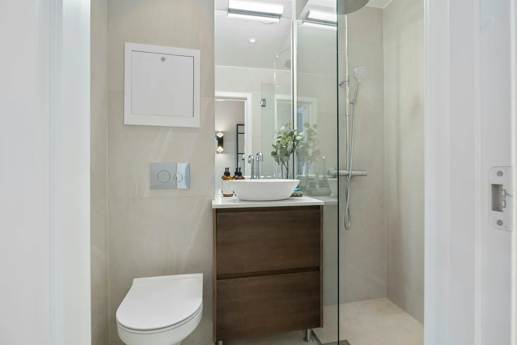 Small modern bathroom renovation in Aurora featuring a wall-hung toilet, a dark wood floating vanity with a vessel sink, and a glass-enclosed walk-in shower with neutral stone tiles.