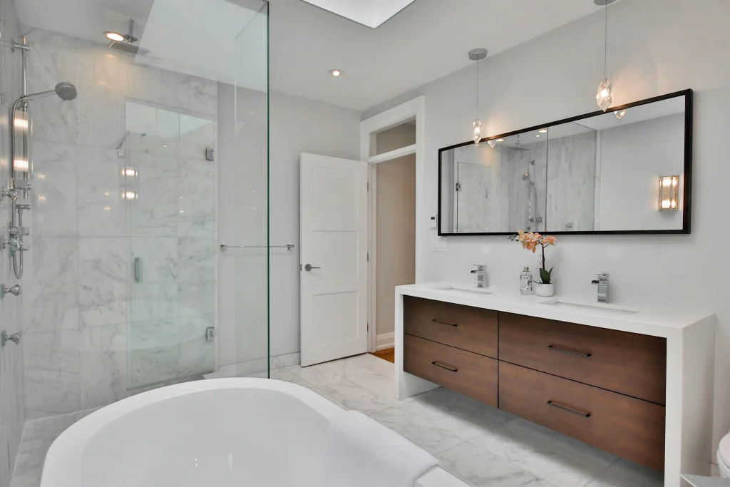Luxury master bathroom renovation in Aurora featuring a marble-walled walk-in shower with a glass door, a custom floating wood vanity with a white waterfall countertop, and a modern freestanding soaking tub.