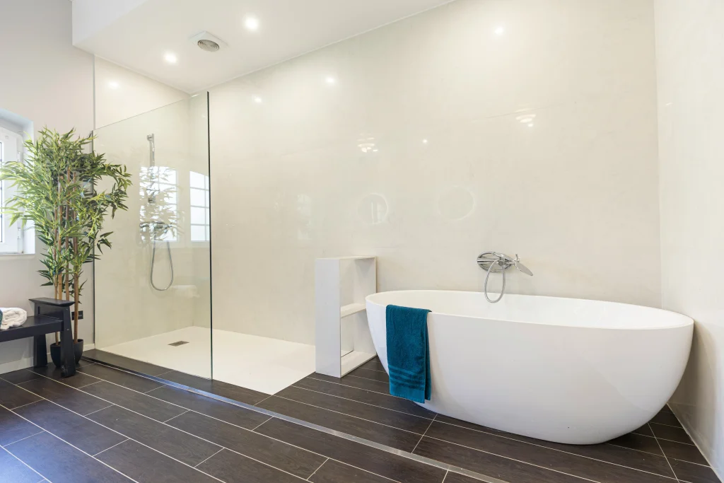 Modern bathroom renovation in Aurora featuring a barrier-free walk-in glass shower, a white freestanding soaking tub, and dark wood-look floor tiles.