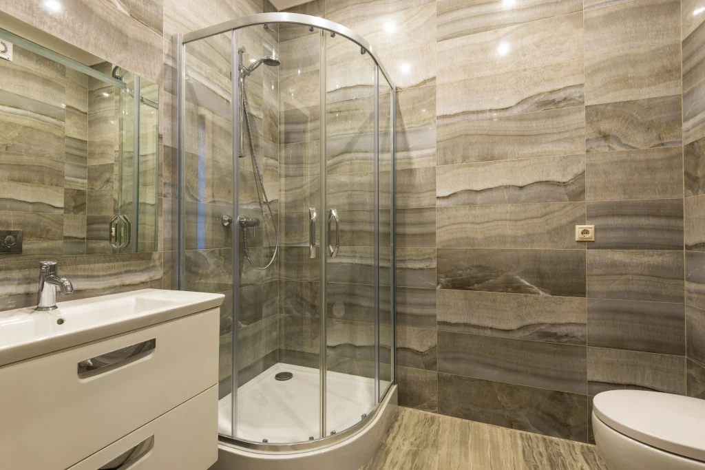 Modern bathroom renovation in Aurora Heights, Aurora, Ontario, featuring a curved glass corner shower stall, earth-toned onyx-patterned wall tiles, and a white floating vanity cabinet.