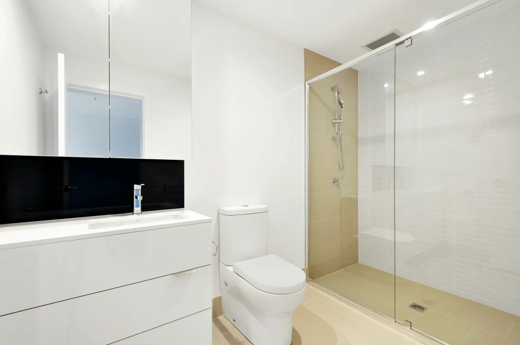 Minimalist basement bathroom renovation in Aurora, Ontario, featuring a white vanity with a bold black backsplash, a frameless medicine cabinet mirror, and a sliding glass shower door.
